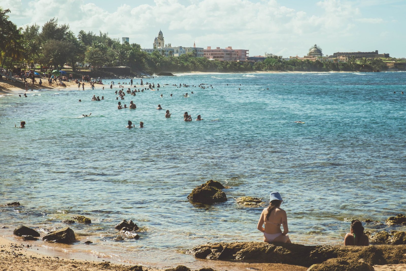 People enjoying the turquoise waters and sandy shores of San Juan's picturesque beach under a clear summer sky.