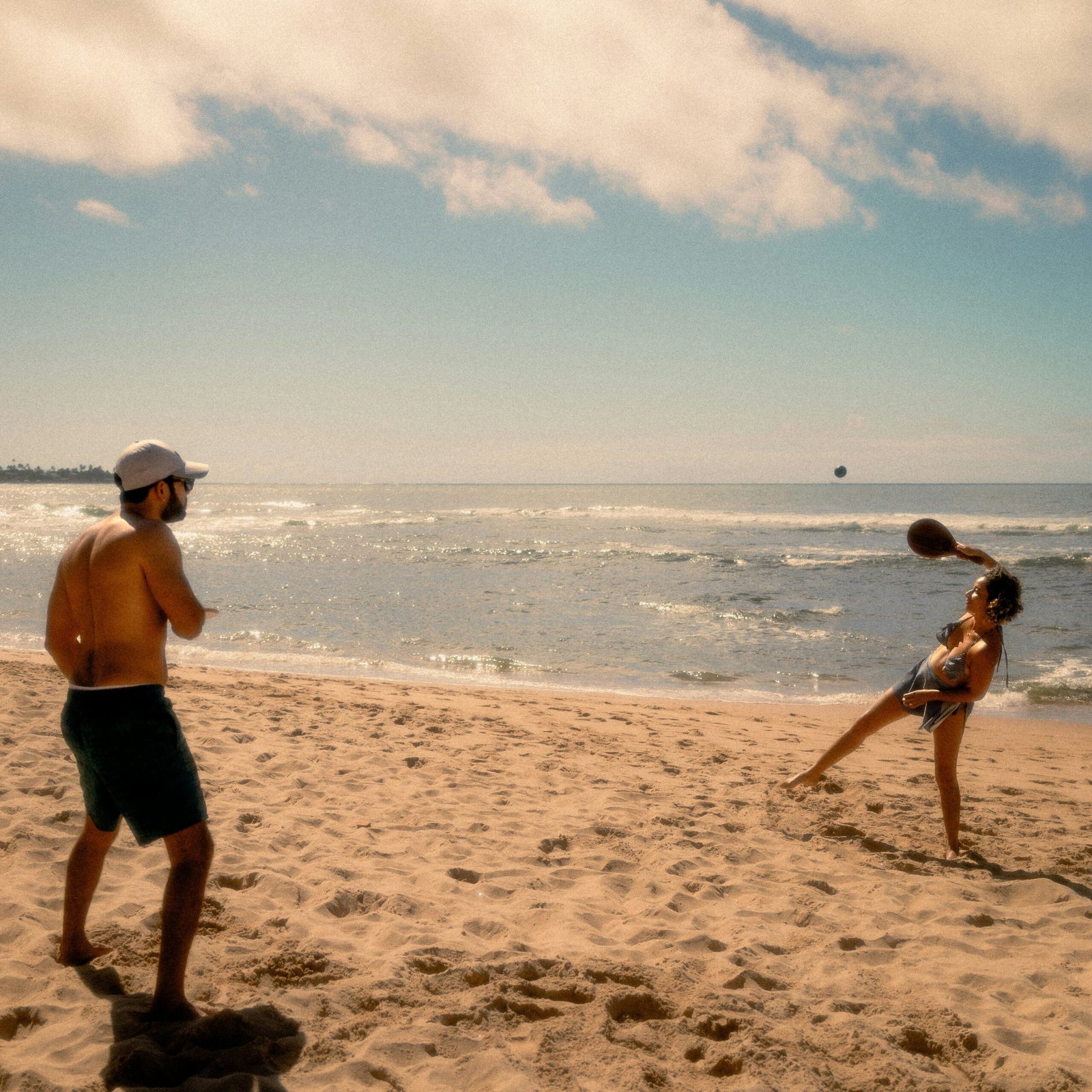 Two adults playing volleyball on a sunny sandy beach, enjoying summer fun.