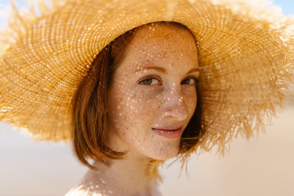 pexels-photo-8760679-8760679 Close-up of a smiling woman with freckles wearing a straw hat outdoors.